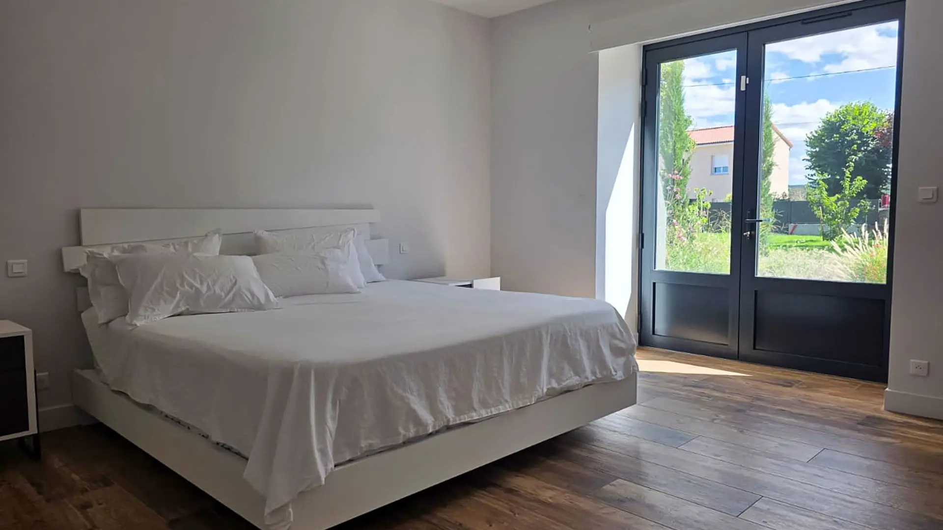 Chambre lumineuse équipée d’une porte-fenêtre en aluminium à double vantail donnant sur le jardin