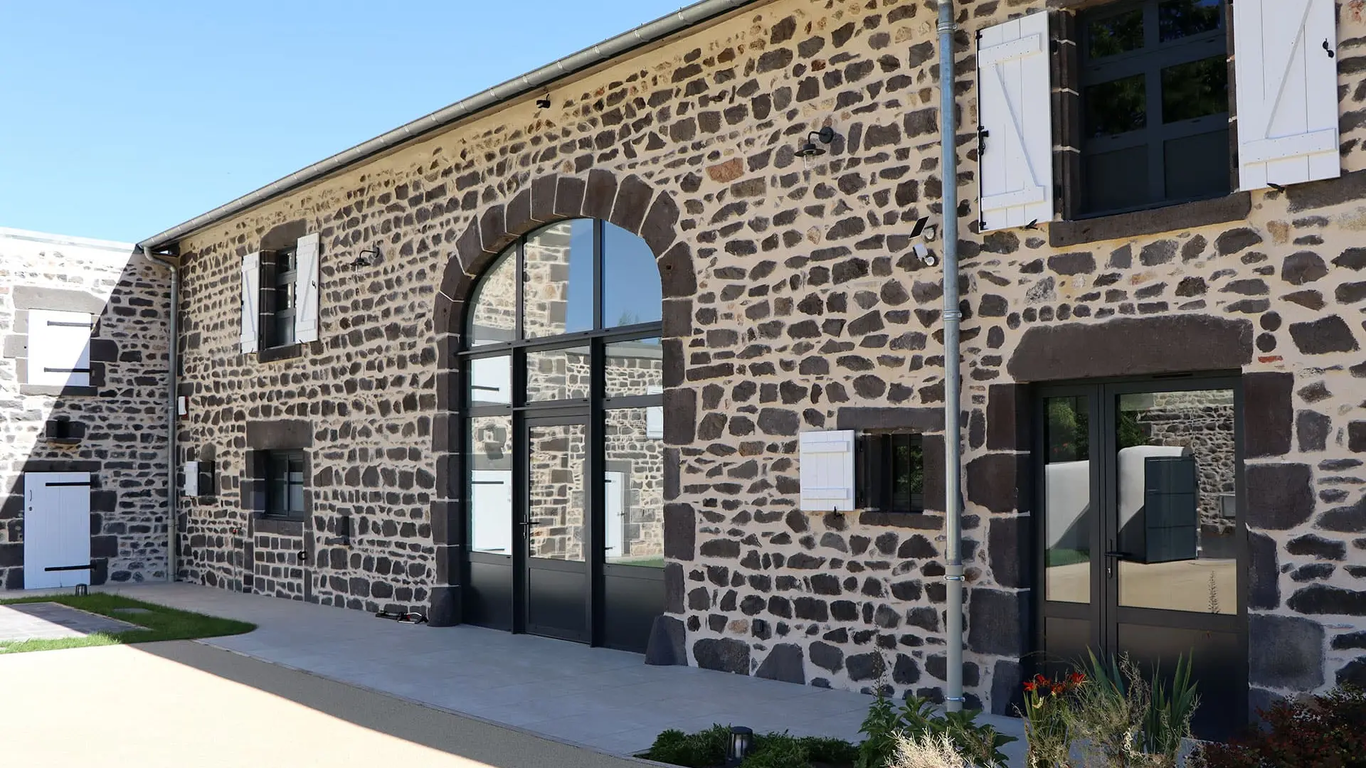 Baie vitrée cintrée en aluminium sur mesure installée dans une ancienne grange en pierre de lave